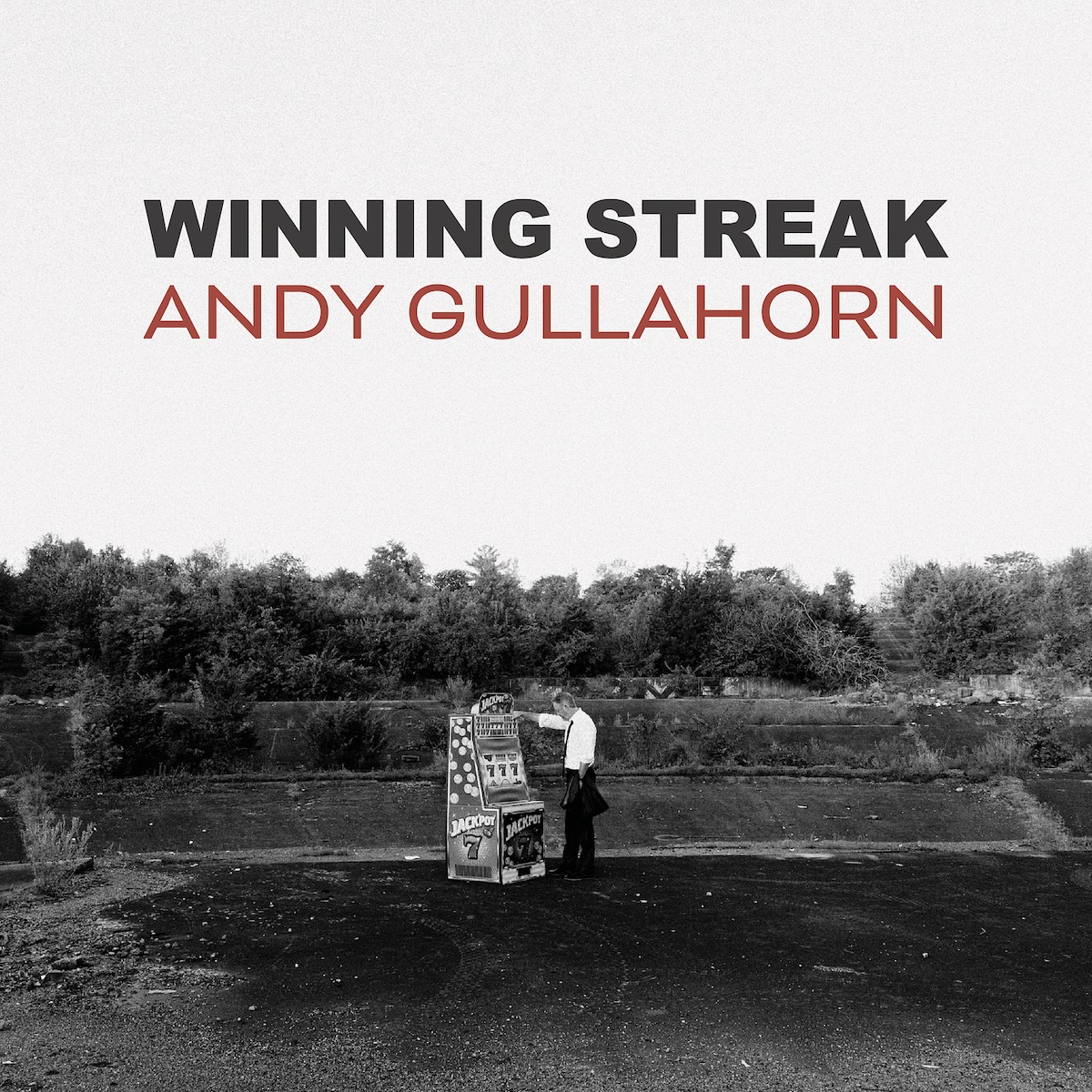 Album Art of Andy Gullahorn's Winning Streak album - A black-and-white photo of an empty flat spot of dirt with some hill and a kind of retaining wall behind it, and woods behind that. In the middle of the center is a man standing in front of a lone slot machine. The top half of the photo is all the white sky, and printed on top of the sky is the album title in large, bold black letters, with the artist's name in thinner, red letters below.