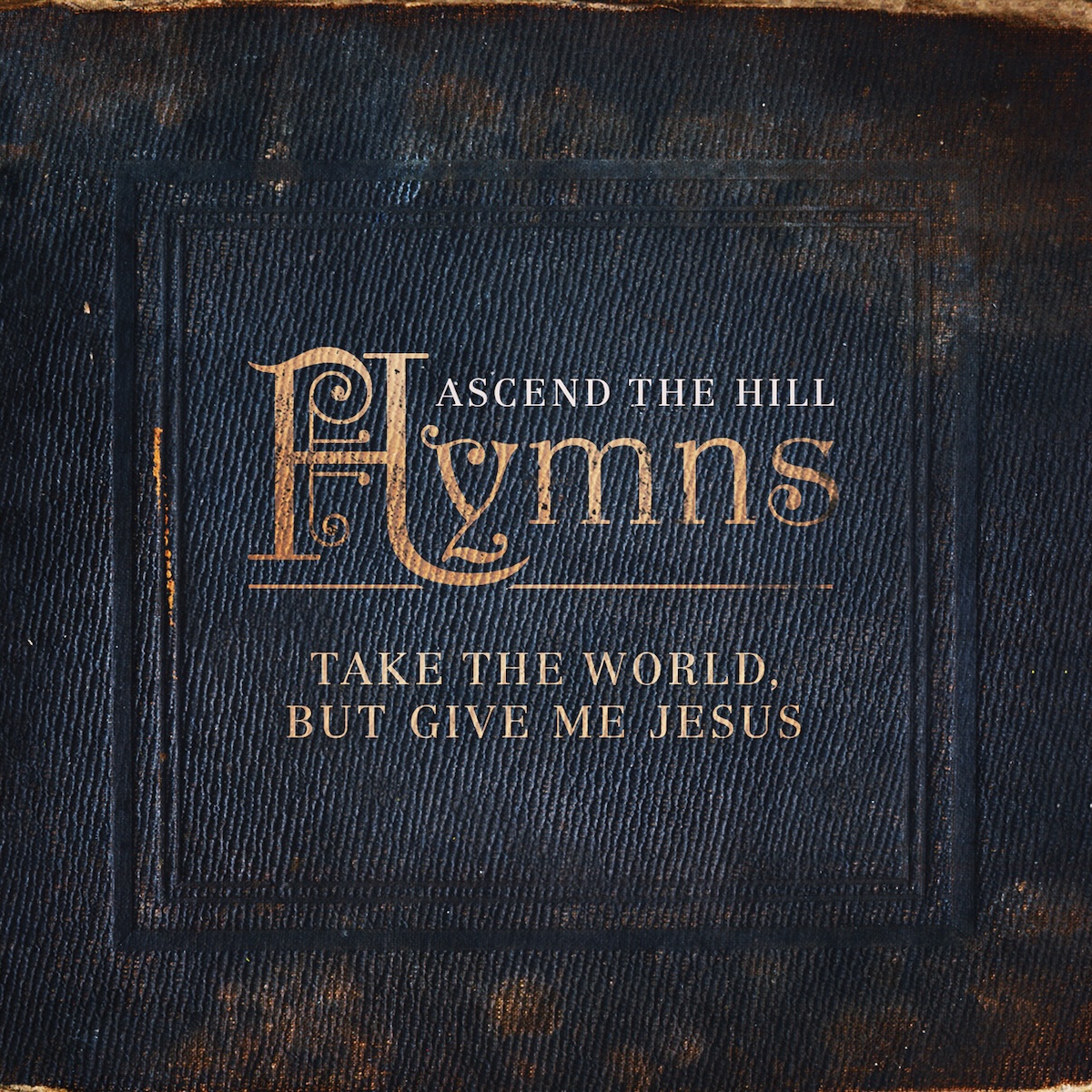 Album Art of Ascend The Hill's Hymns album - A square photo that looks like the cover of a square, leather-bound book. The cover is very worn on the edges and has a blue, textured look to it. Inside a few leather borders in the middle is a large, ornate, gold-hued 'H' and the letters 'ymns' are smaller next to it to spell out the album title. Below that, in smaller gold print is 'Take The World, But Give Me Jesus' album subtitle. Above the tile is the band's name in small white print.