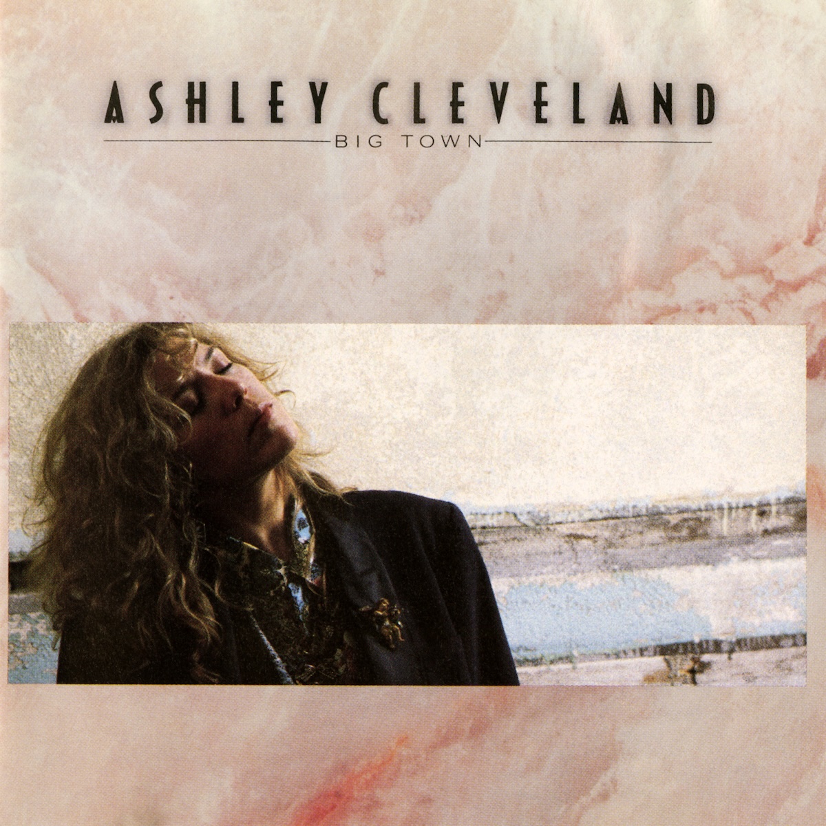 Album Art of Ashley Cleveland's Big Town album - The background looks like some sort of pink and white marble stone. Across the bottom of the middle is a wide photo of a young woman with long, light brown curly hair. he's wearing a black coat and and has her eyes closed and has a contemplative look on her face. She seems to be sitting next to a wall with some odd horizontal holes in it.</body></html>