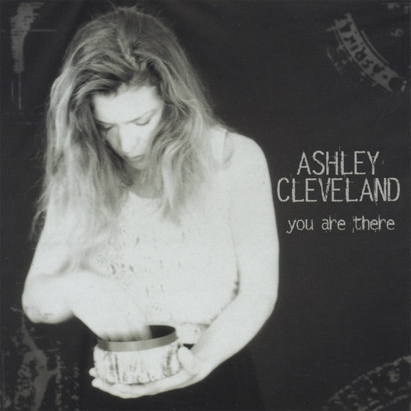 Album Art of Ashley Cleveland's You Are There album - On a black background, a black-and-white photo of a woman with long, brown-blond hair who is holding in her left hand a metal tin of some sort and ruffling through it with her right hand. The right of her is printed her name in large, uppercase gray letters. Below that, in smaller lowercase letters, the album title.