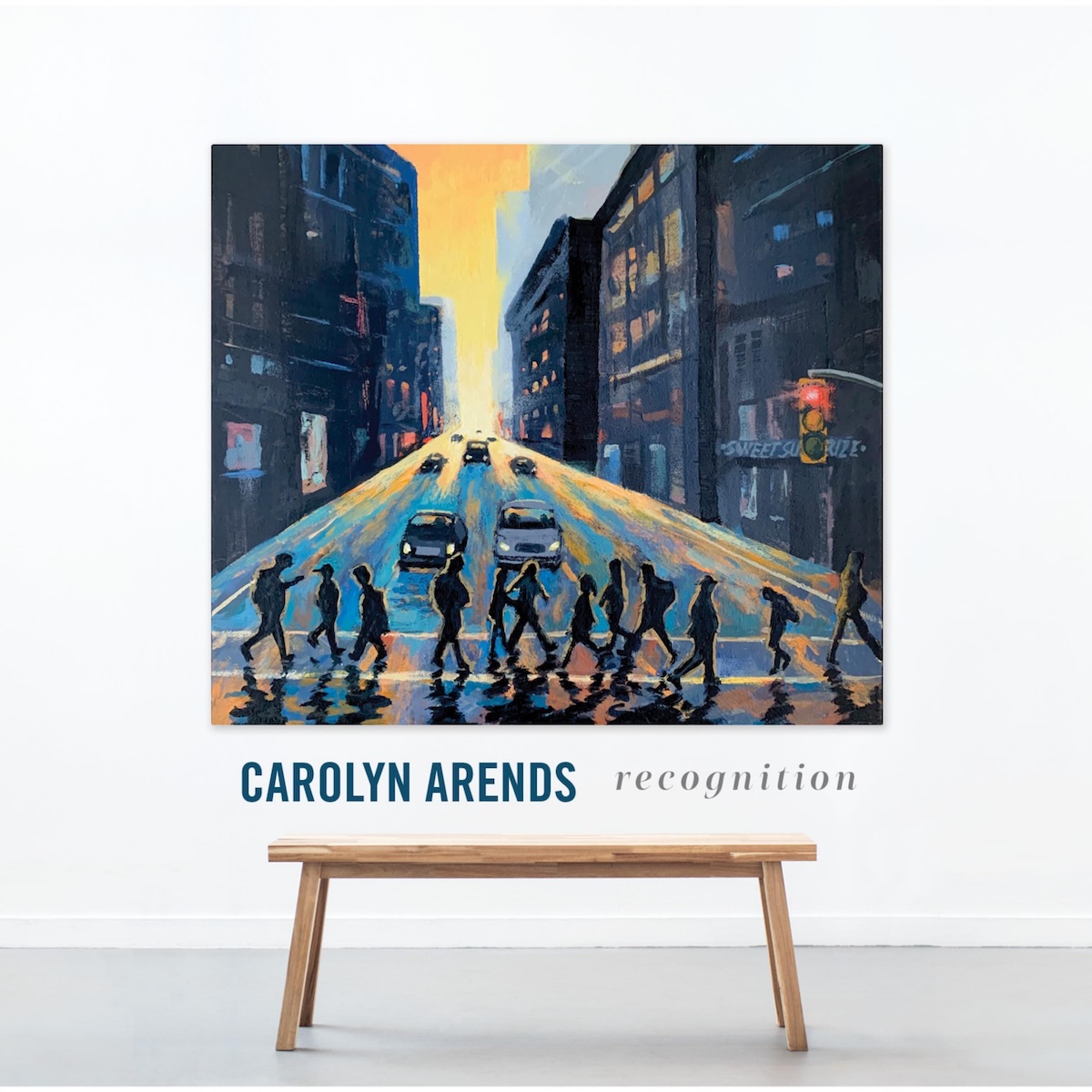 Album Art of Carolyn Arends's Recognition album - A photo of a white wall with a grey floor at the bottom. On the floor is a wooden bench in front of a painting mounted on the wall. The painting is wider than the bench and almost as tall as it is wide. It's a painting of a street in a city with multi-story buildings lining the side of the road. The sun is setting in the background and it's lighting up the road.</body></html>