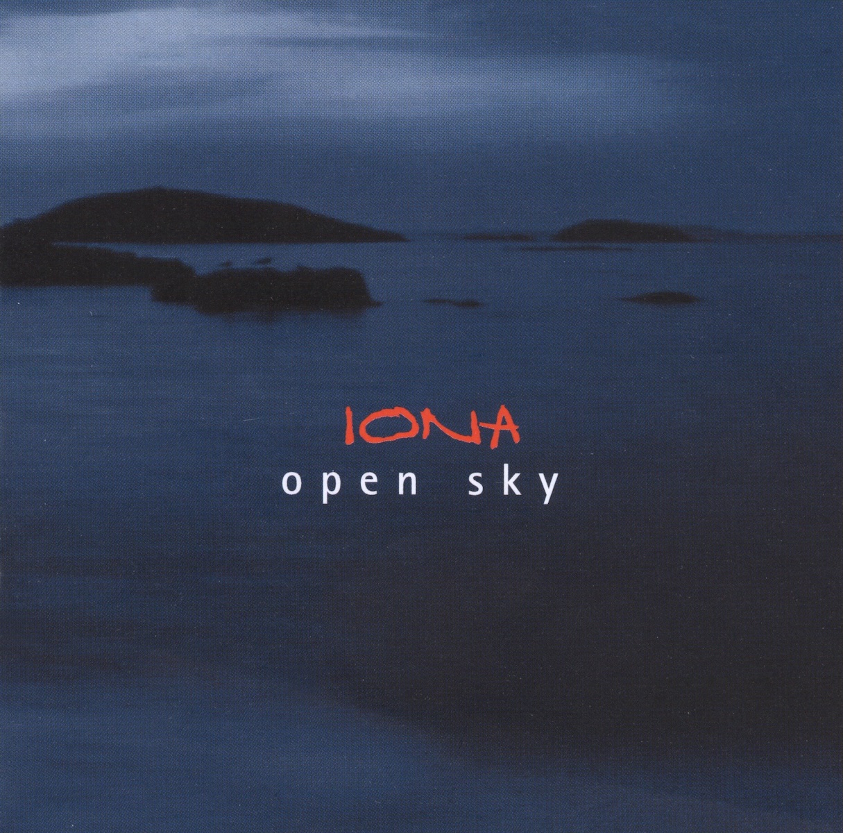Album Art of Iona's Open Sky album - A photo that is mostly dark blue; a photo of a series of small rocky outcroppings and islands silhouetted on a dark blue/gray sea. In the sky above, there are pockets of light shining more than the darker clouds. It looks like it could be taken at dusk or pre-dawn. In the middle, in a handwritten font in red is the band's name, and below it in white is printed the album name.