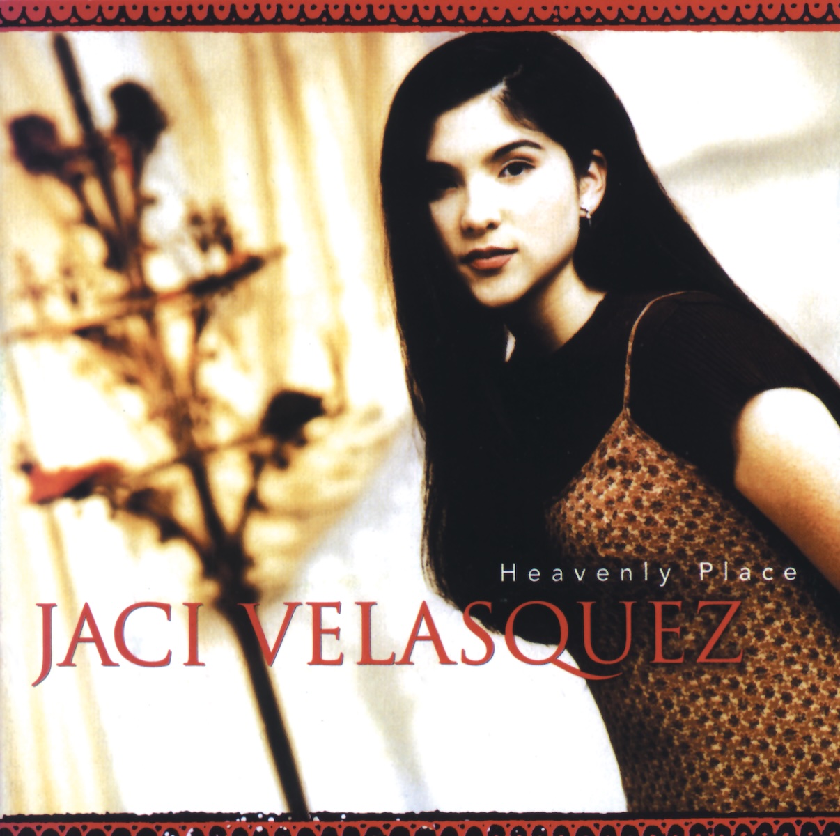 Album Art of Jaci Velasquez's Heavenly Place album - In a well-lit room, a photo of a teenage girl with long, black hair and a brown patterned dress is shown on the right side, with some sort of circular stand and curtains behind her on the left, though out of focus. The woman is looking at the camera and looks petite with a slight smile. Towards the bottom of the photo her name is printed in large red letters, with the album name in much smaller white letters above her name on the right.</body></html>