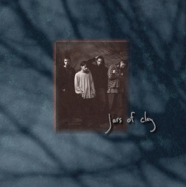 Album Art of Jars Of Clay's self-titled album - The majority of this is a dark blue background that looks like branches being photographed through sunlight and very blurry. In the middle is a black-and-white is 4 white men, most of them in baggy clothes and not looking at the camera. In the bottom right of that photo is the handwritten band name with a drop shadow above both the photo and the background.