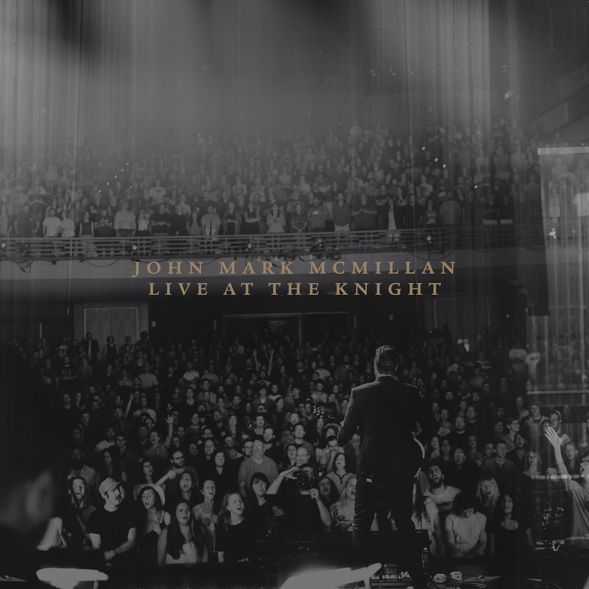 Album Art of John Mark McMillan's Live At The Knight album - A black-and-white photo of a man on a stage in the foreground, facing away from the camera and towards an audience. He's wearing a suit coat and holding a guitar. The audience is on the floor and on a balcony, hundreds and hundreds of people. Obscuring the video on the top and on the right is some sort of light refracting in the lens or some sort of effect to make it look cooler, mostly vertical lines of light.</body></html>