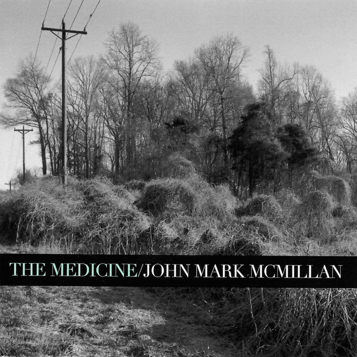 Album Art of John Mark McMillan's The Medicine album - A back and white photo of tall grasses in the foreground, bushes in the middle ground, and bare trees in the background, with a power line cutting through the left of the frame and a grey sky. Printed on top of the photo at about a quarter of the height from the bottom is a black line with the album title printed in a powder blue, a '/' and then the artist name in a light grey.