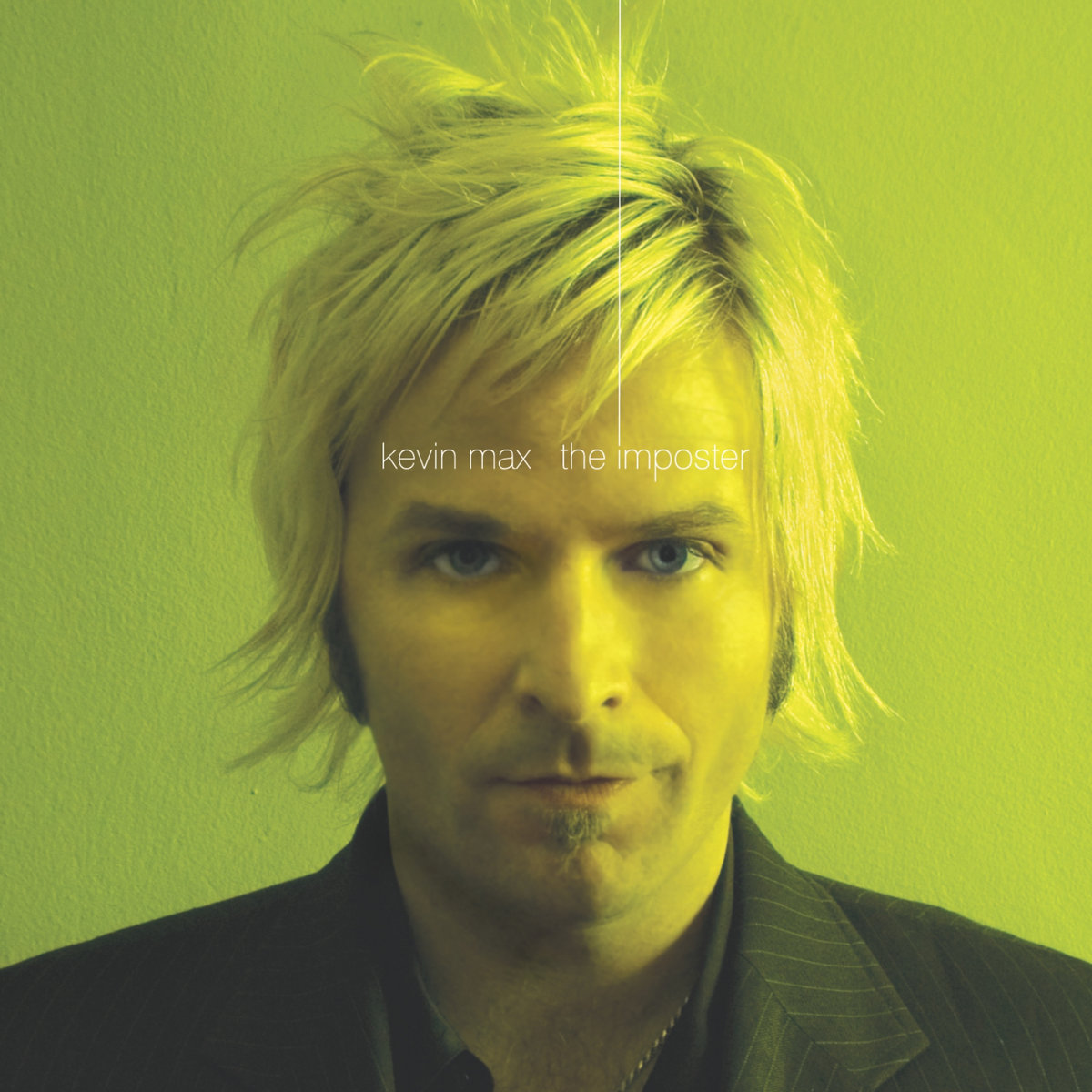 Album Art of Kevin Max's The Imposter album - A photo of a white man with bleached blonde hair that is a few inches long is dressed in a black pinstripe suit and photographed from the shoulders up. He's standing front of some bright green background and there's a golden light to the right of frame illuminating his face. On top of his forehead is printed in white in a very thin, sans-serif font first the artist name and then after a big space the album name.