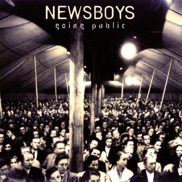 Album Art of Newsboys's Going Public album - A black and white photo of thousands of people standing inside a very large tent the size of a gymnasium or larger. They are facing the camera and looking a bit off to the right of the camera. There seems to be lights set up in the ceiling of the tent to light up the scene and there are a bunch of support poles that break up the sea of people a bit. From the dress of the people, the photo may be from earlier in the 20th century, though it seems to have electric lights so it's not too old. At the top, the band name is printed in large, thin white print, with the album title in much smaller letters below the band name.