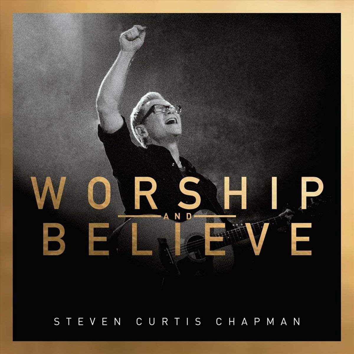 Album Art of Steven Curtis Chapman's Worship And Believe album - A somewhat grainy black-and-white photo of a middle-aged man standing holding a guitar and holding his right hand up in praise while looking upwards with his mouth open and eyes closed, maybe in the middle of singing. The man is lit but the background is mostly dark and is probably a hazy stage. Above where his guitar is, it says in large letters the album title in a gradient that is gold in the top right and a darker golden brown in the bottom left. Also, a thick border around the edge is also that golden to brown gradient. At the very bottom in smaller, white letters is printed the artist's name.