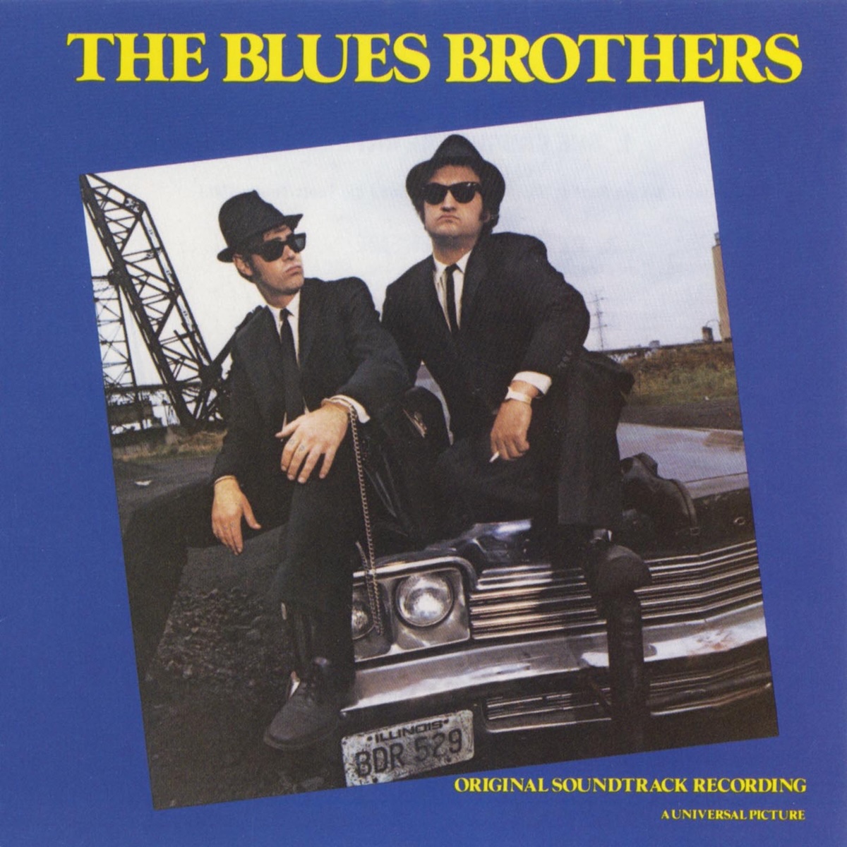Album Art of The Blues Brothers Soundtrack album - On a solid blue background, a square photo of two men is in color but also rotated about 10 degrees off center counter-clockwise. The photo shows two white men in black suits and pants with thin black ties and tall black hats, also wearing sunglasses.</body></html>