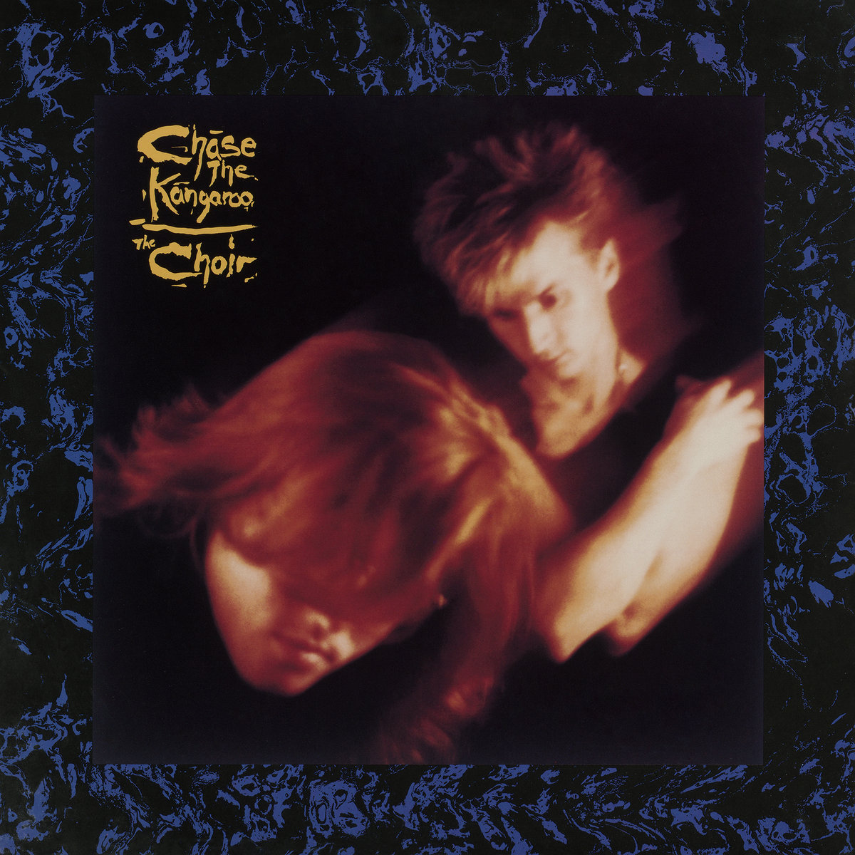 Album Art of The Choir's Chase The Kangaroo album - A thick border of black with blue drawings making an indecipherable pattern surrounds the main photo. The main photo is one man on the left leaning in towards the camera and his hair is in front of his eyes. The second person is off to the right further away, and is holding his own shoulders and lookng down. Both people are slightly blurry like they were photographed in motion. In the top left of the photo is the album title and the artist name written in a handwritten manner in a mustard yellow.