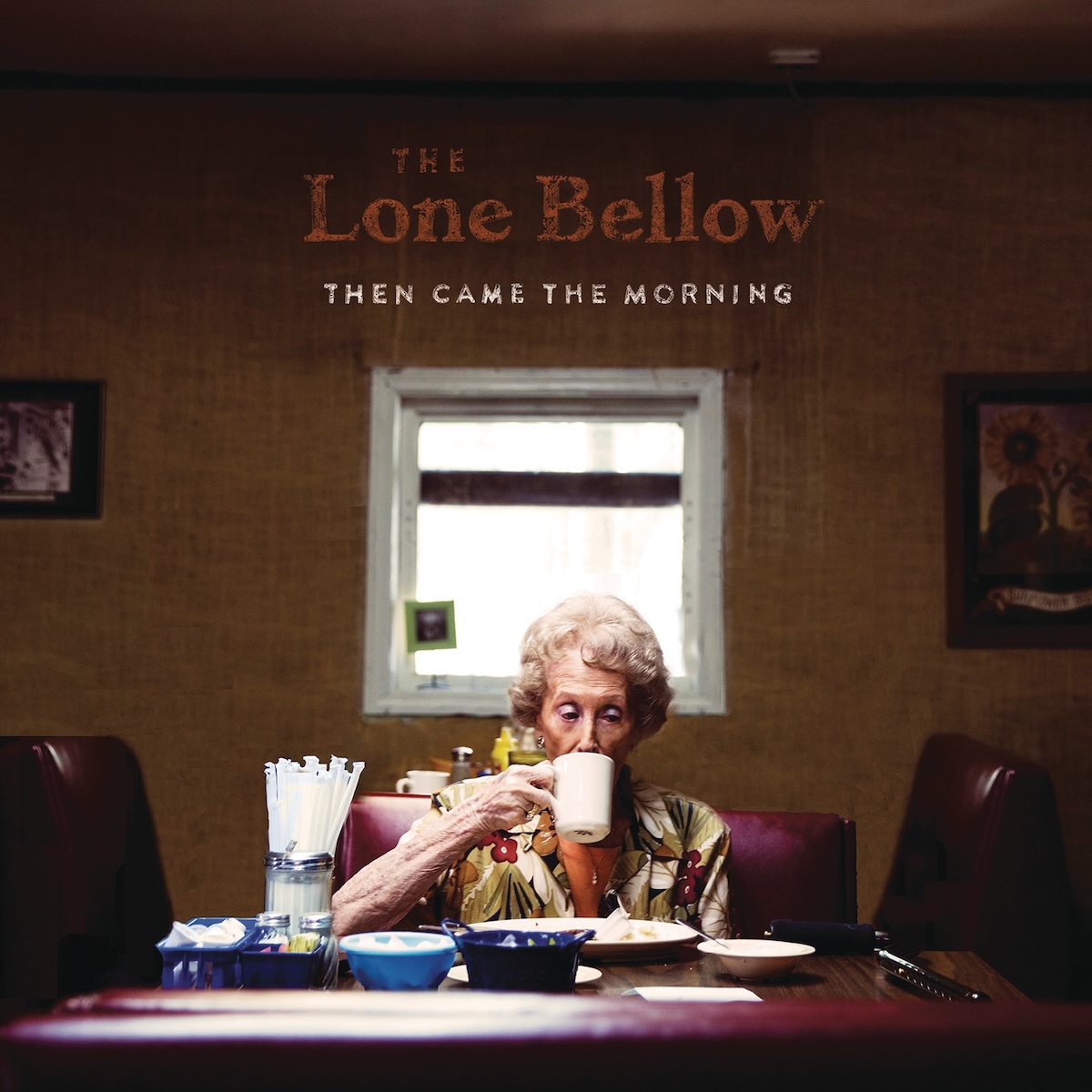 Album Art of The Lone Bellow's Then Came The Morning album - A photo of an older woman with white, permed hair sitting on the other end of a small table at a restaurant is sipping on a cup of coffee. She seems to be sitting by herself and have mostly finished a plate of food as it looks mostly empty. On the table are a couple empty side platters, a large jar with straws and a few other small bowls or trays with various condiments.</body></html>