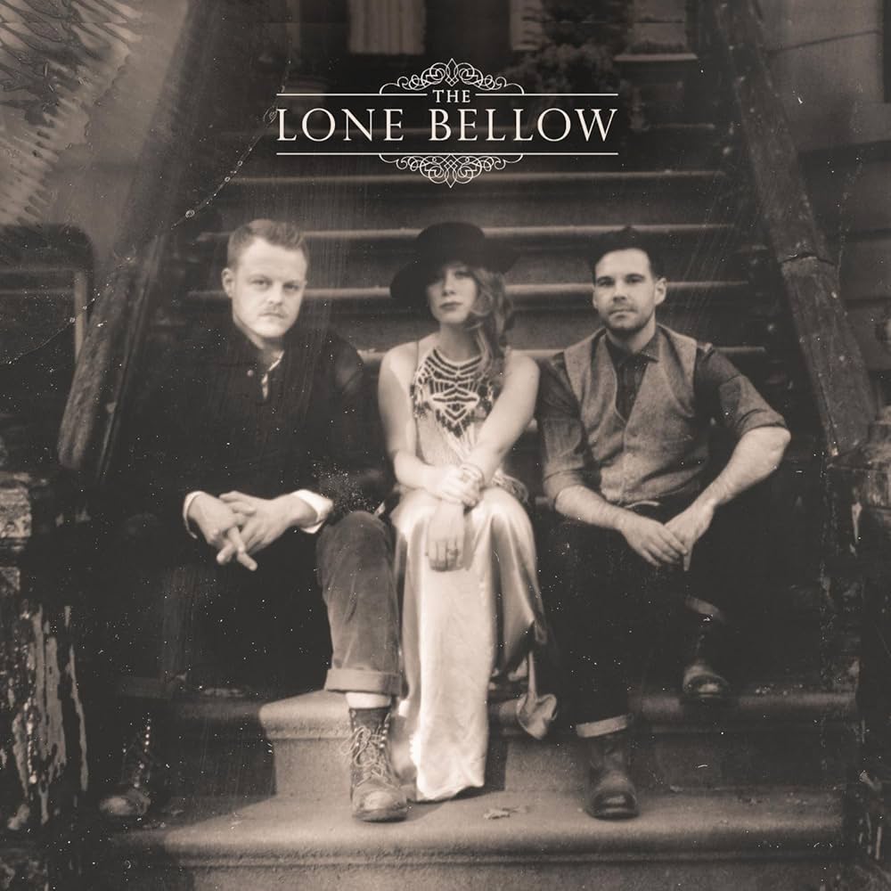 Album Art of The Lone Bellow's self-titled album - In a black-and-white photo, three white people are sitting on the front steps of a New York City brownstone, from the looks of it. On both the right and left are men wearing boots, the one on the left with lighter hair and a black shirt, and the one on the right with black hair and a grey shirt with vest and black pants. In the middle is a woman with probably brown hair coming down over her right shoulder. She's wearing a light-colored dress with no sleeves and beadwork on the chest area. They look really classy and somewhat timeless, though I think their clothing is modern. Above them, printed in white is the band name, with 'The' being smaller and built into a decorative line art above the rest of the name, with a similar line art right below the name.