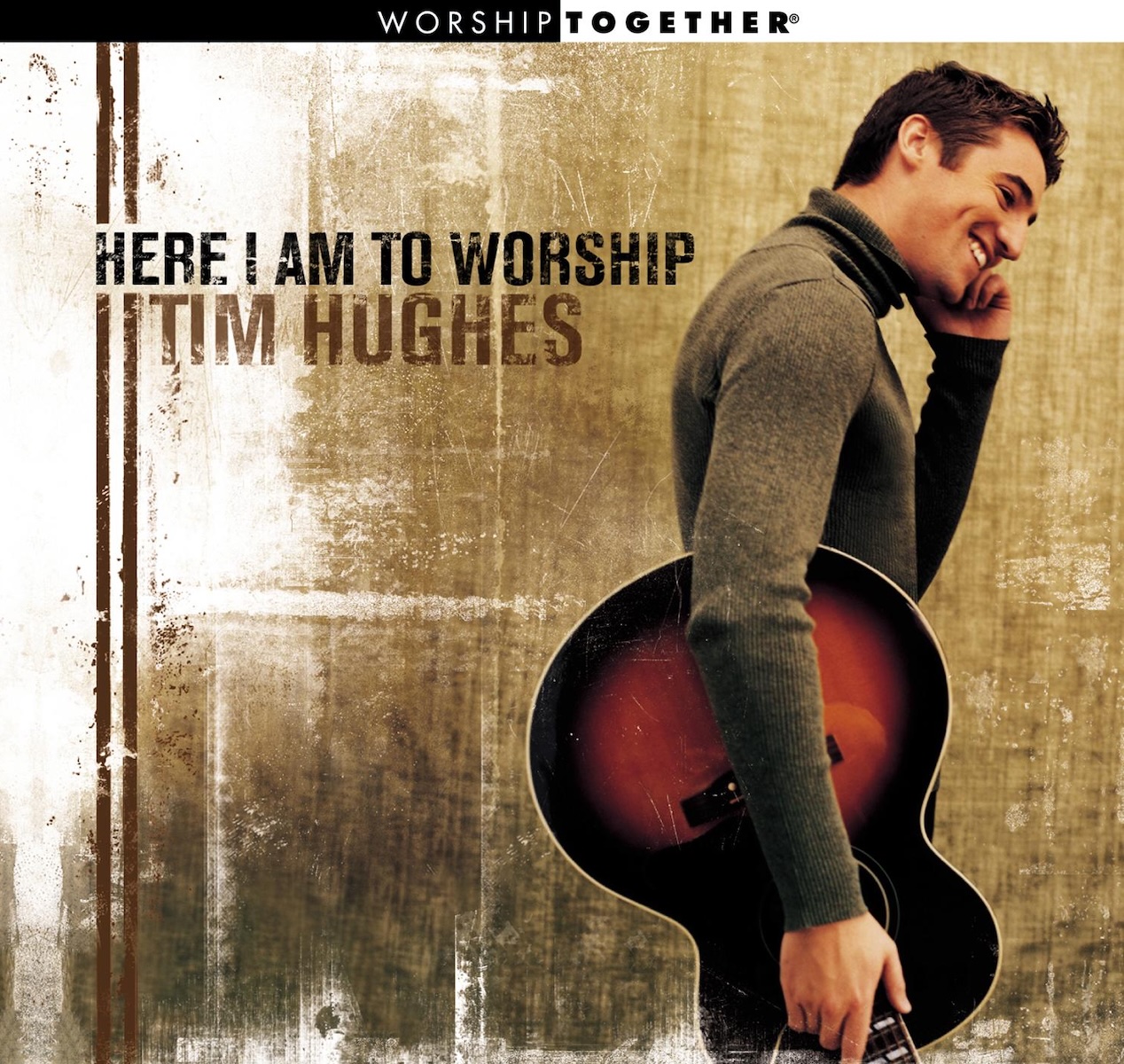 Album Art of Tim Hughes's Here I Am To Worship album - A young man with short brown hair and a long-sleeve grey turtleneck has an acoustic guitar on his right hip with the neck facing down, and he's smiling and looking down to the right of the frame. The background is brown mottled texture with some white paint thrown on top of it, and two vertical brown lines printed above that.</body></html>