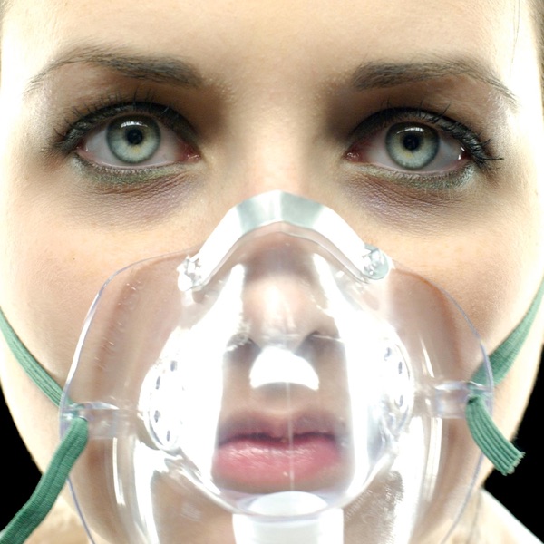 Album Art of Underoath's They're Only Chasing Safety album - A close up photo of a woman's face, it looks like in front of a black background. There are no hairs in front of her face, and it's so close we cannot really see her scalp. The lighting is very bright and sterile from the front, though her eyes are in shadow a bit. Her mouth and nose are covered by a clear plastic mask held on her head by aqua green elastic straps going behind her head on both sides. Her facial expression is blank and her eyes are a very light green/gray color.