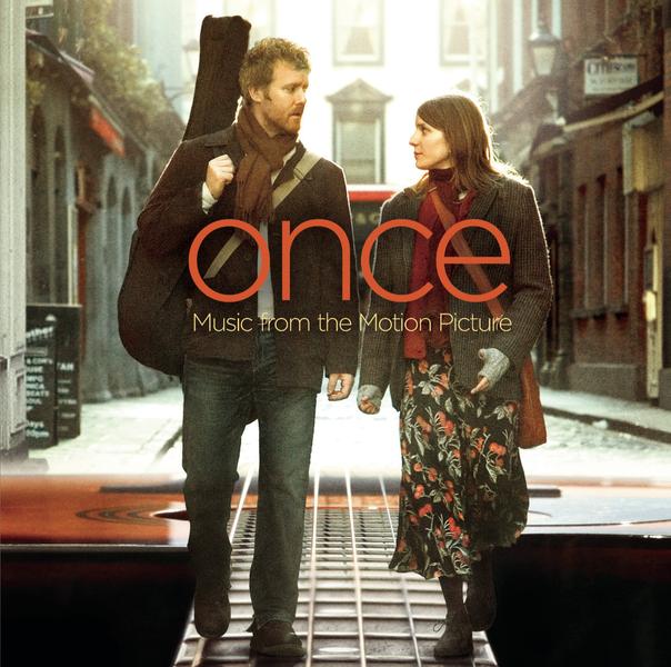  Music From The Motion Picture album - A photo of two people on a cobbled side street in a European city, walking and talking. The man has a guitar in a case on his back and the woman is gesticulating like she is making her point. The bottom of the background street is replaced with a photo of an acoustic guitar looking down the neck of the guitar towards the main part of the guitar. Printed in the middle in red is the movie title in lower case, with 'Music From The Motion Picture' in much smaller text below it.